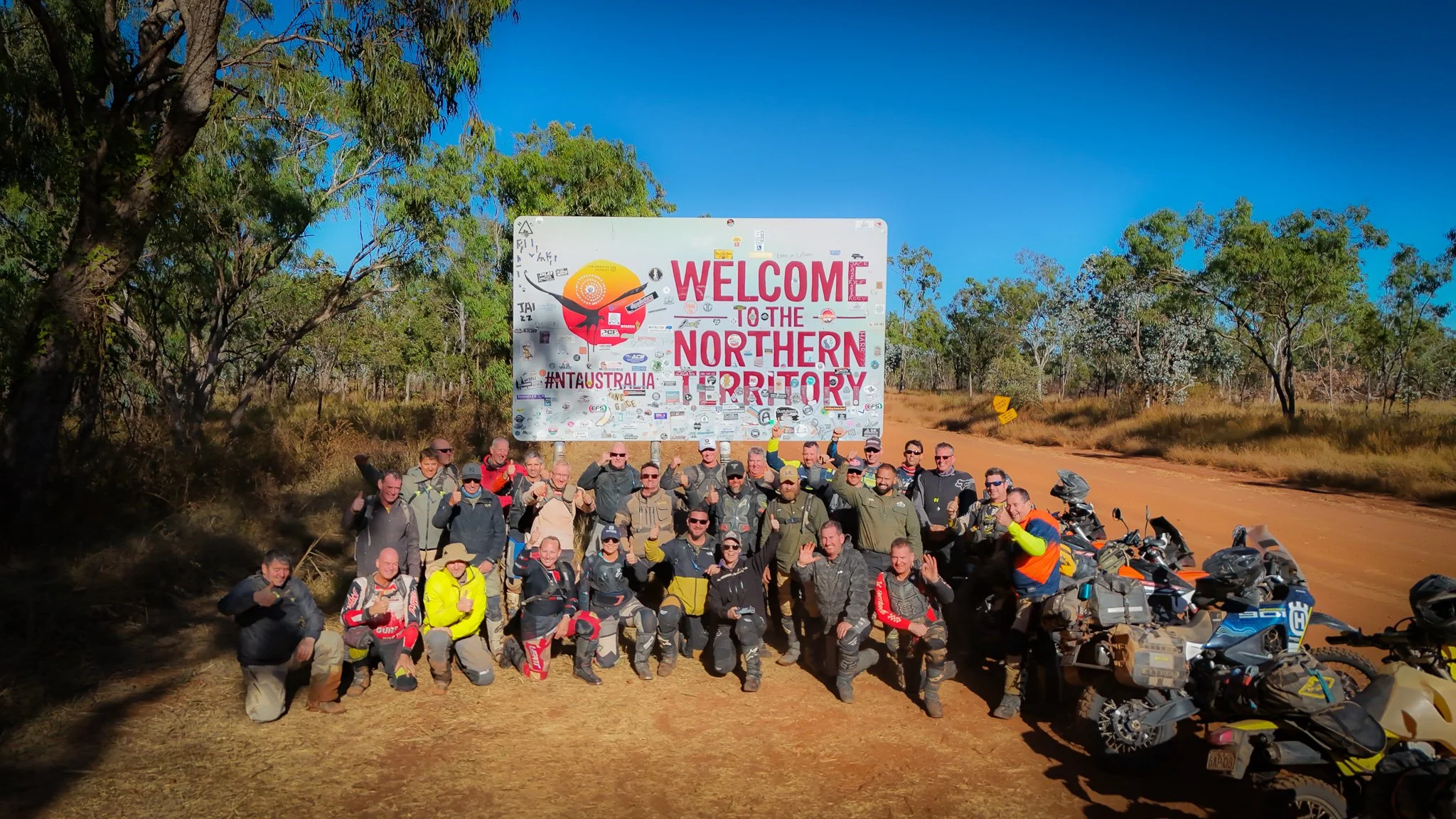 Cairns to Darwin motorcycle tour group photo at Northern Territory border on Savannah Way