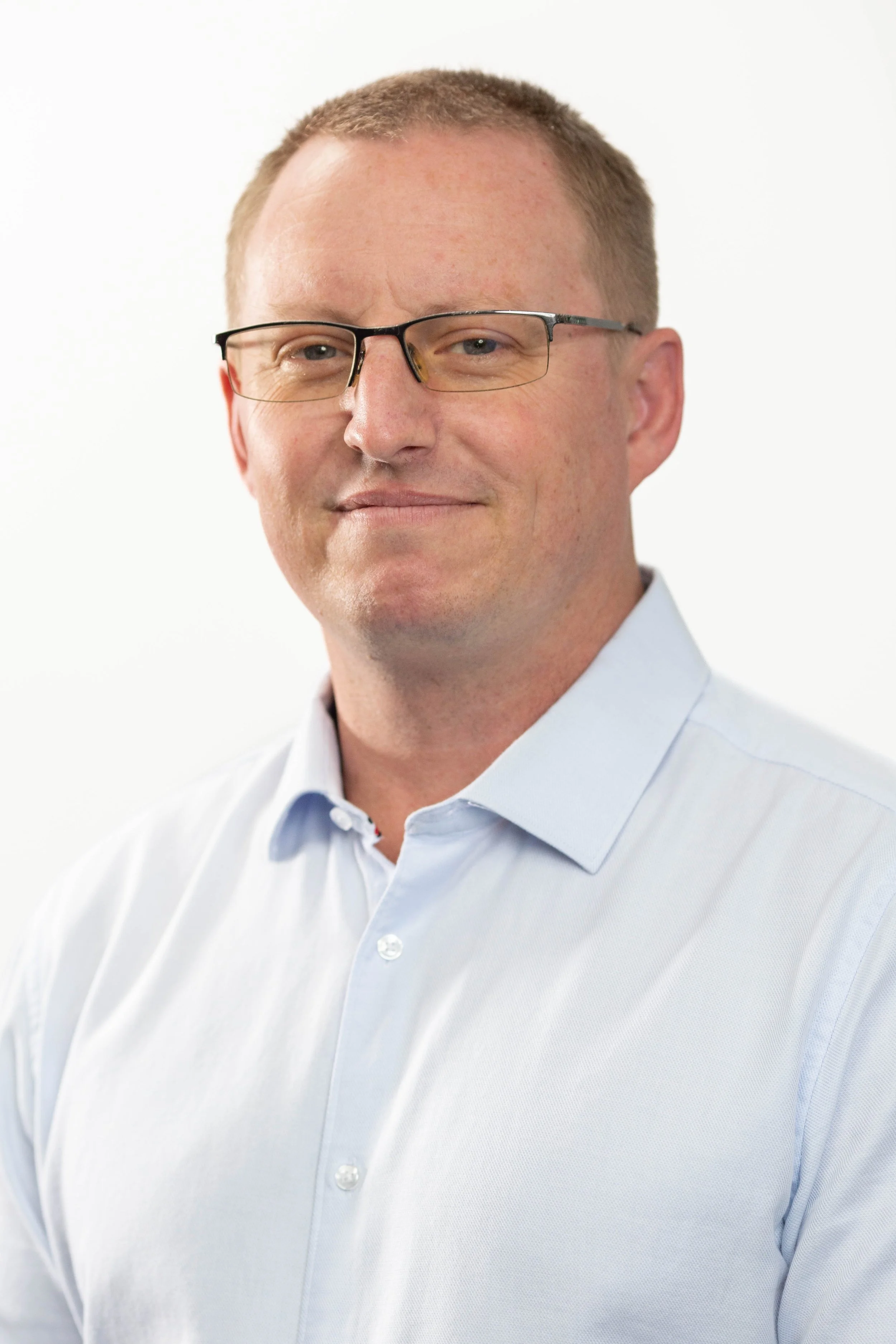 Headshot of a man with glasses wearing a white collared shirt, smiling slightly, against a plain white background.
