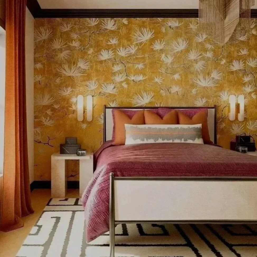 A modern bedroom with a yellow wall featuring white floral patterns, a bed with pink pillows and a white and gray patterned pillow, a beige rug with black geometric design, and wall-mounted white lights on either side of the bed.