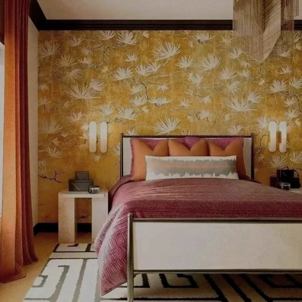 A bedroom with a gold floral wallpaper, a white and black bed with burgundy bedding and multiple pillows, gold and white wall sconces, marble side tables, and burnt orange curtains.