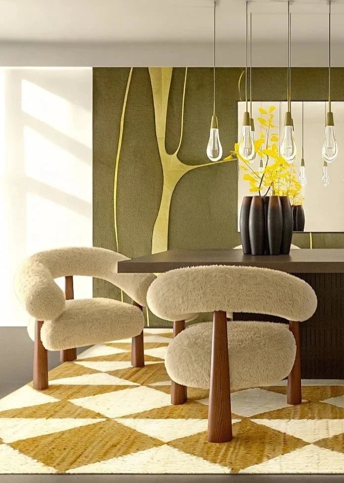 Modern dining area with a dark table, cream plush chairs, a yellow and white geometric rug, and a dark wall with abstract art. Hanging light bulbs and yellow floral arrangement in black vases also visible.