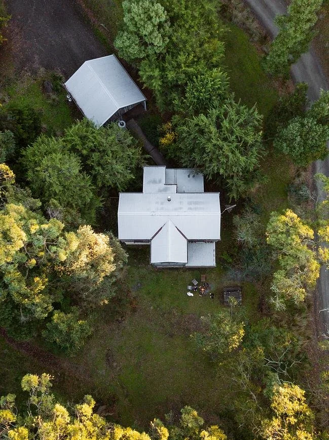 Aerial view of a house surrounded by trees with a small outbuilding nearby.
