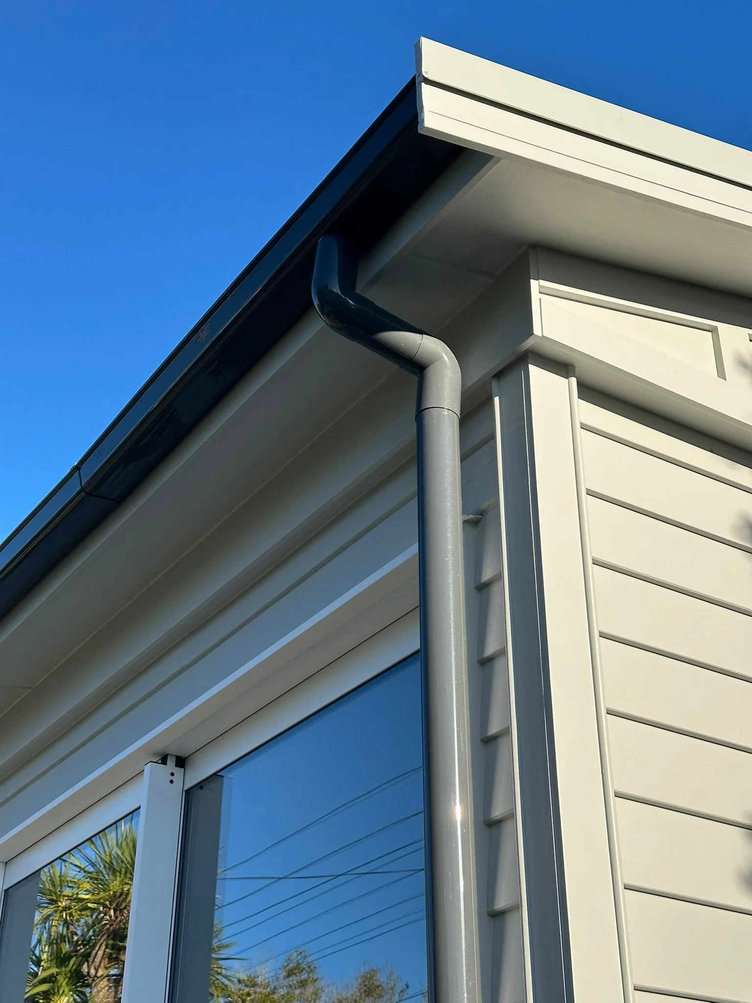 Close-up of the corner of a newly renovated house showing the roof, gutter, downspout, and cladding