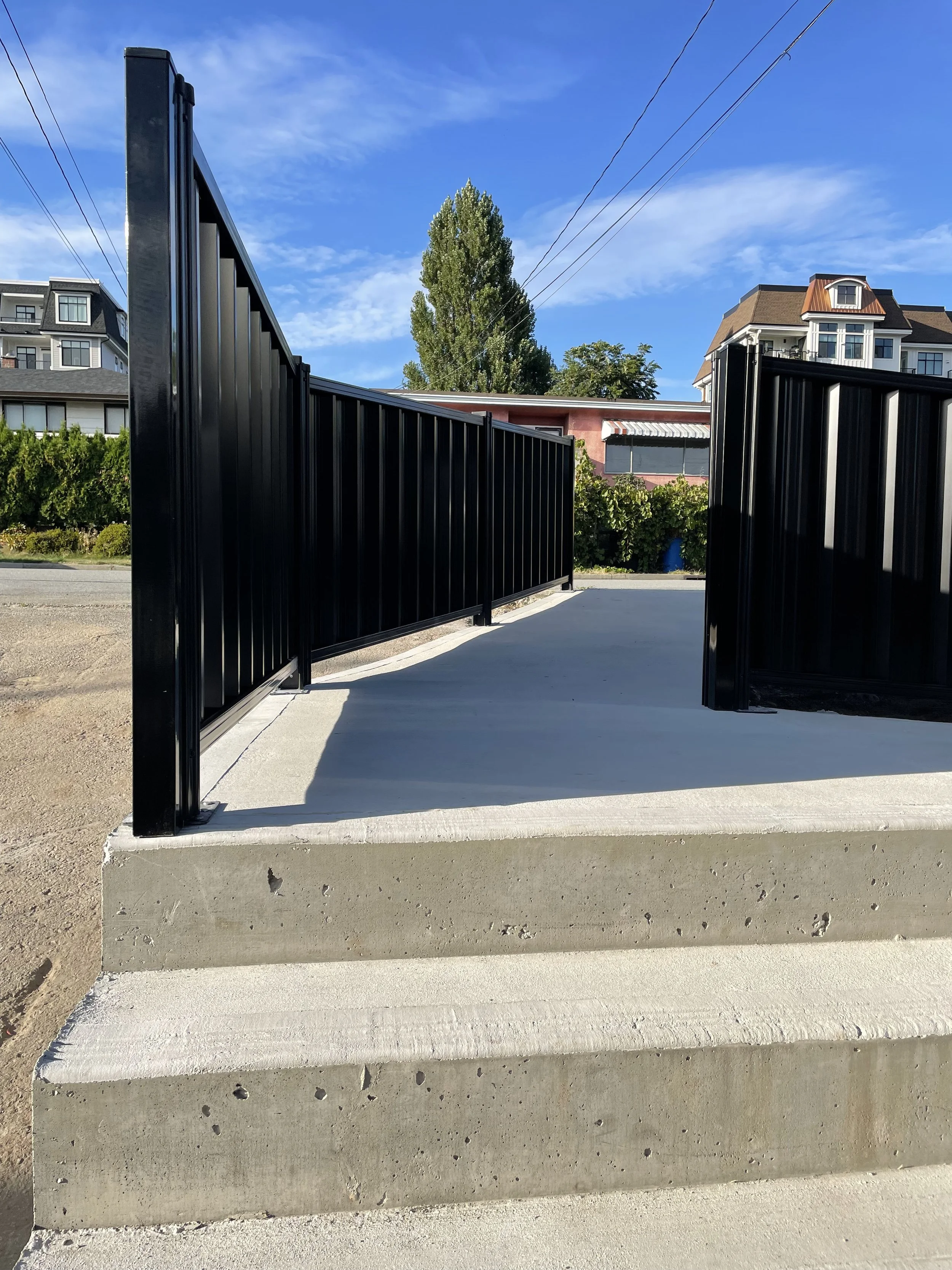 Concrete steps leading to a pathway with black metal railings, under a clear blue sky.