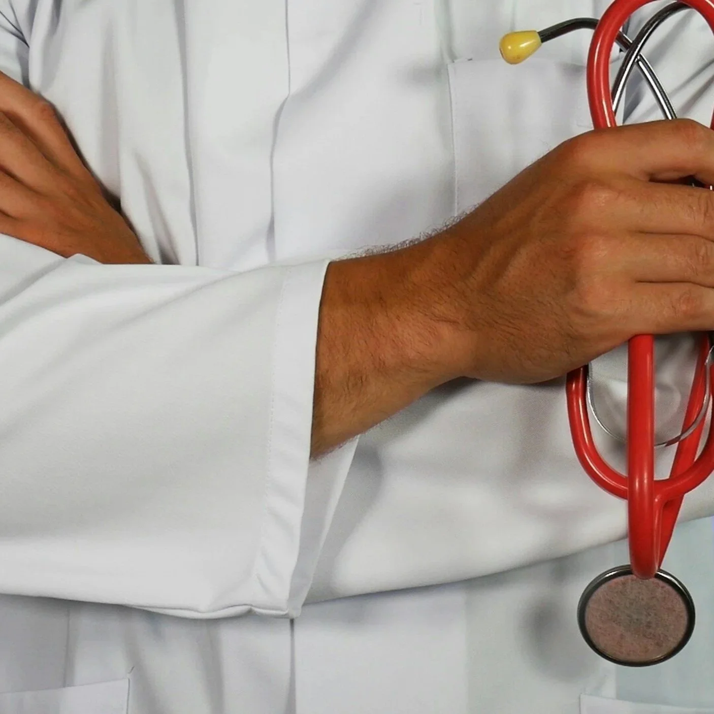 Close-up of a healthcare professional's hand holding a red stethoscope, wearing a white lab coat.