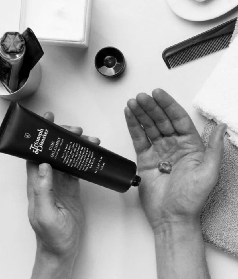 Person holding Triumph & Disaster tube with cream on hand, razor, comb, towel