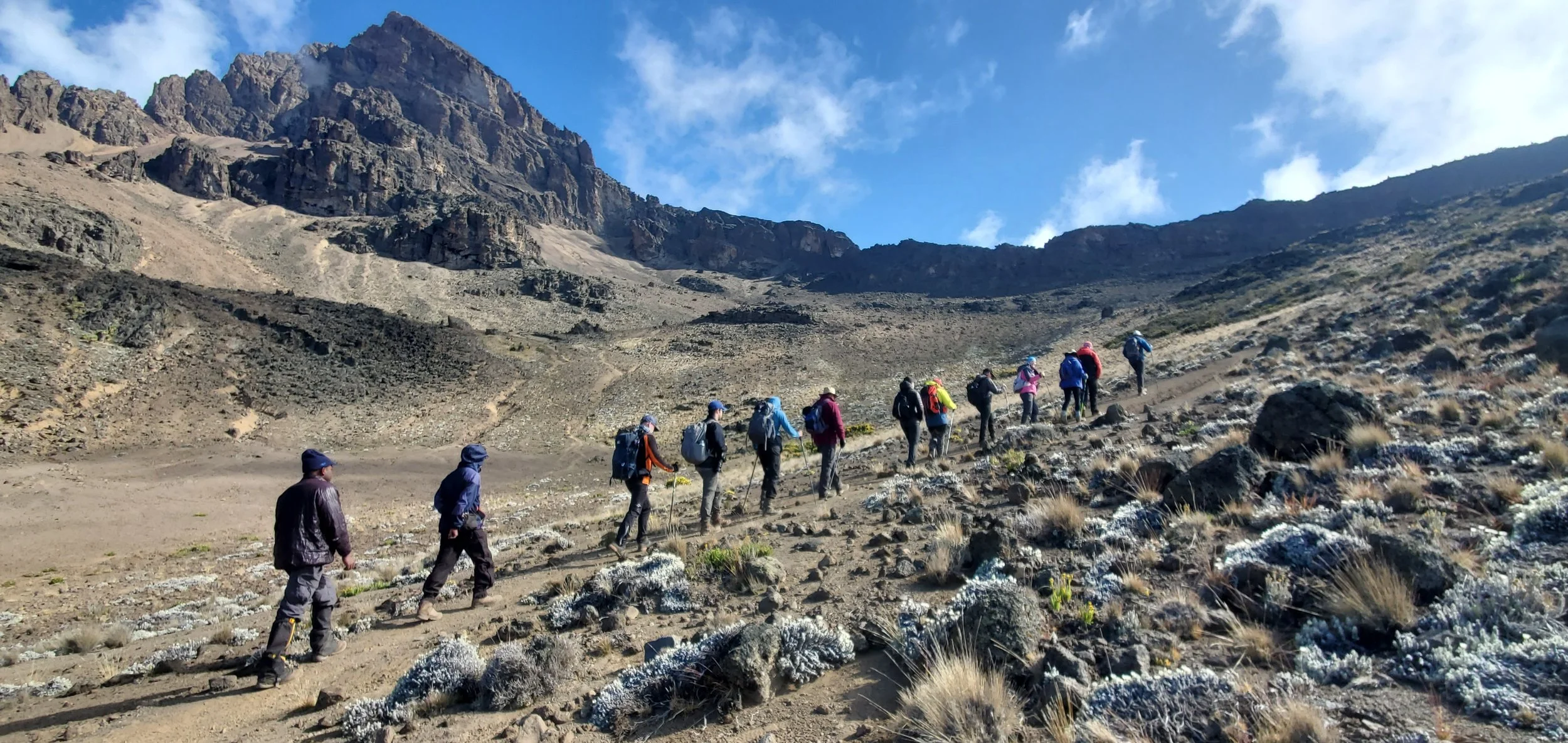 A group of hikers climbing a rocky mountain trail under a partly cloudy sky.