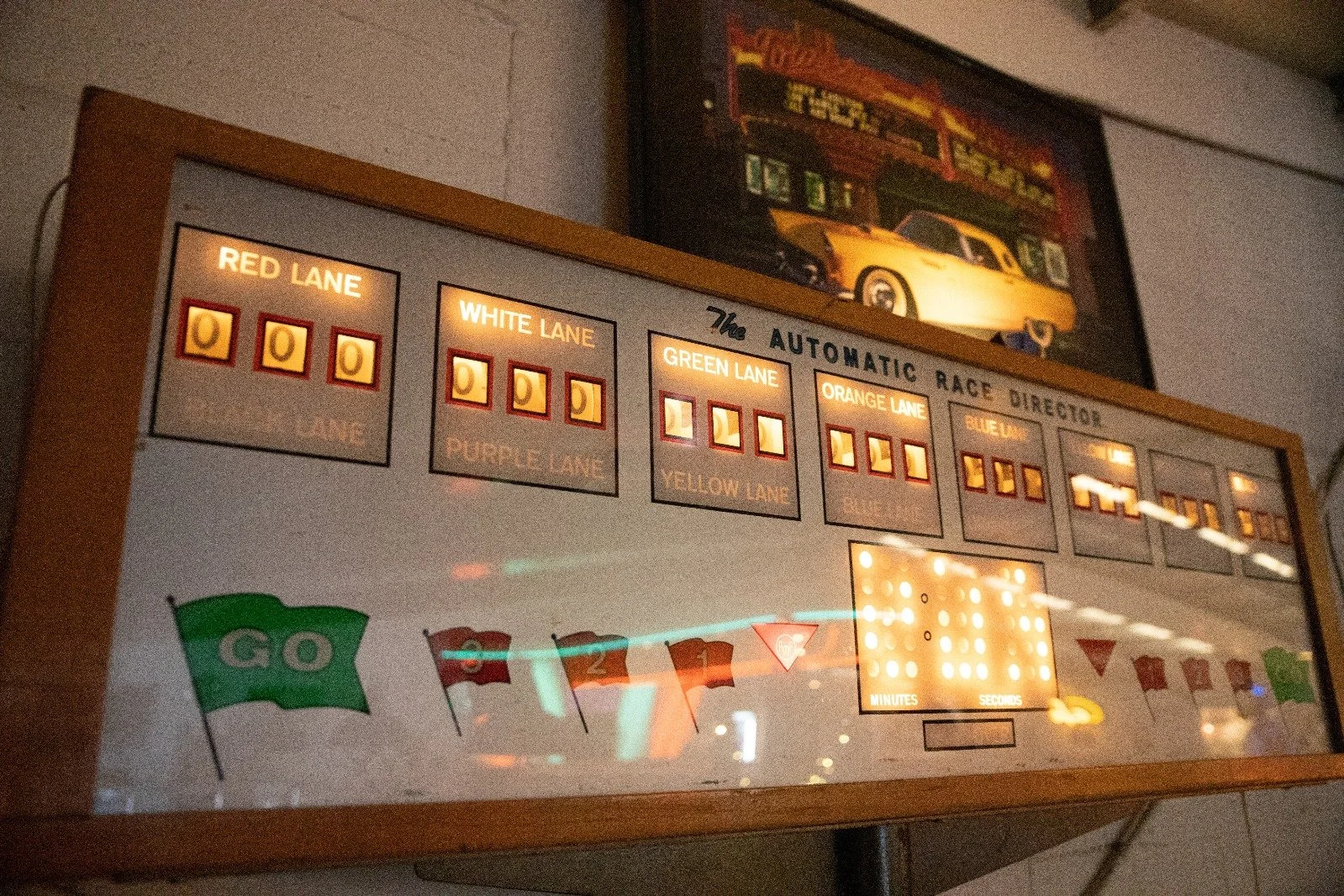 Ein elektronisches Race-Director-Board zeigt die Startaufstellung mit verschiedenen farbigen Spurenzonen und einem Countdown. Es trägt die Überschrift 'The Automatic Race Director' mit Bezeichnungen für die Spurfarben und Zeitangaben.