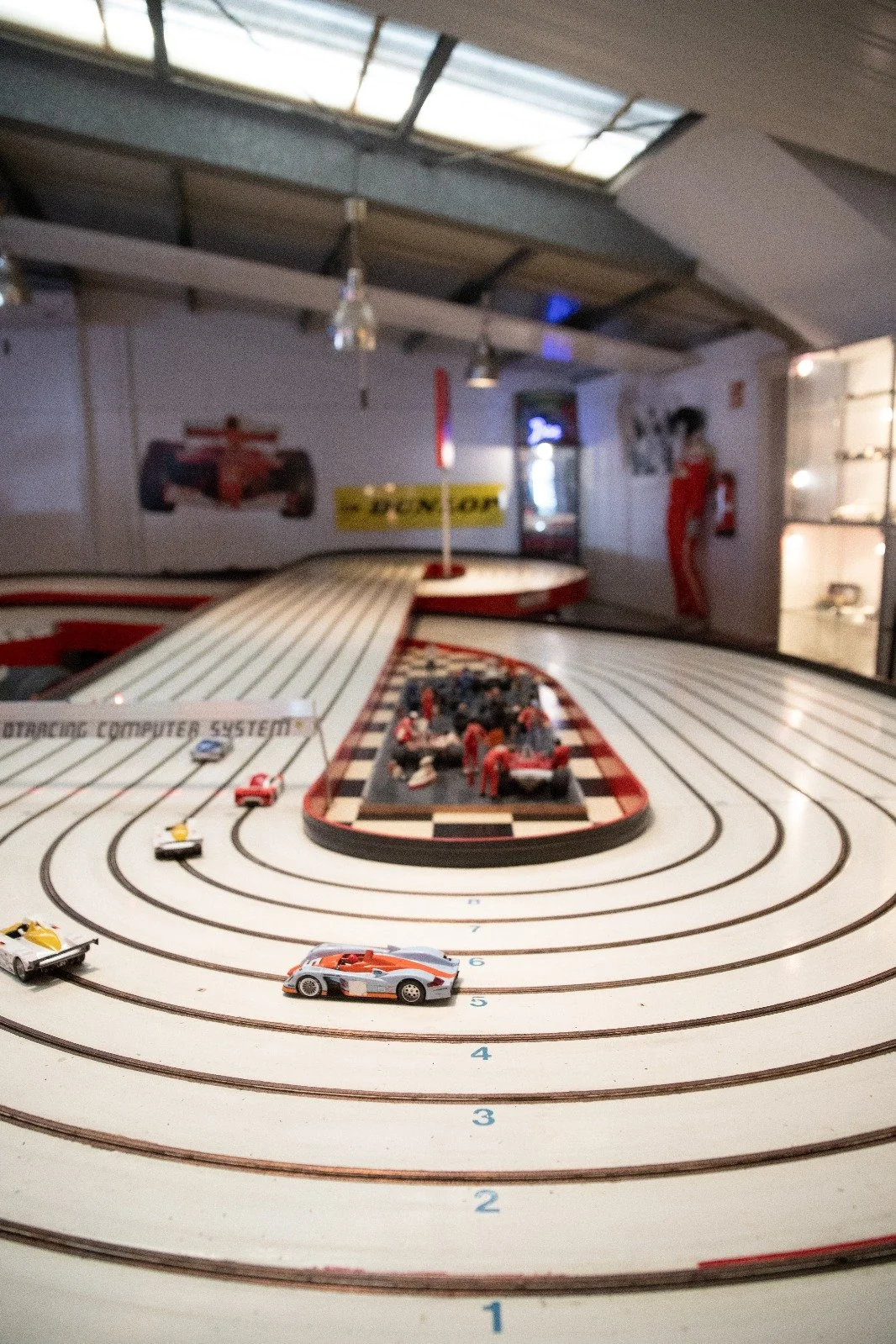Miniaturrennstrecke mit Spielzeugautos, Rennbahn mit mehreren Spuren und Rennfigur, im Hintergrund Poster eines Formel 1 Autos, Rennsitzer und Diorama. 