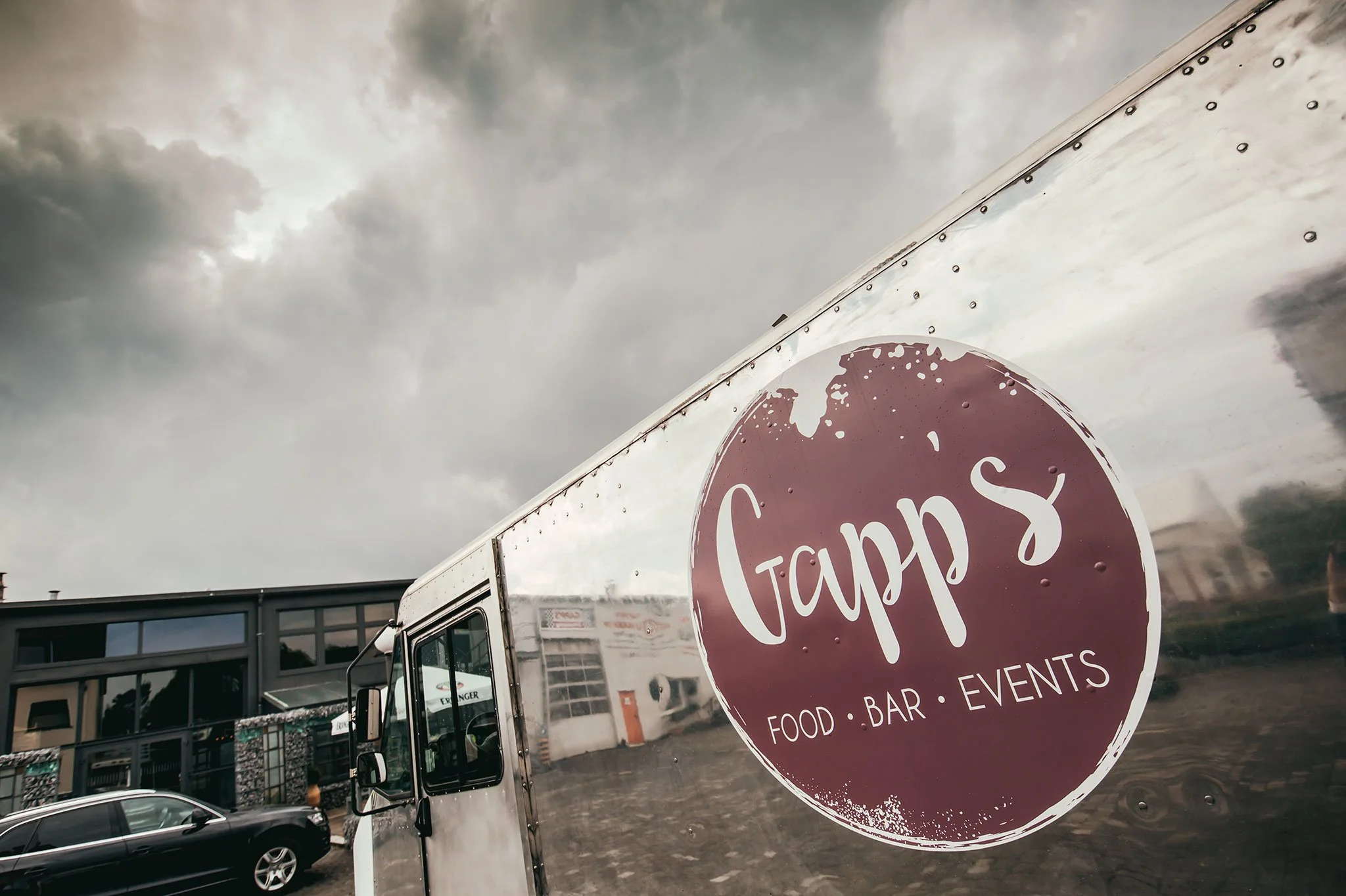 Ein Reflektor mit einem runden Aufkleber, der den Namen 'Gapp's' und die Wörter 'Food', 'Bar' und 'Events' trägt, auf einem Fahrzeug bei bewölktem Himmel.