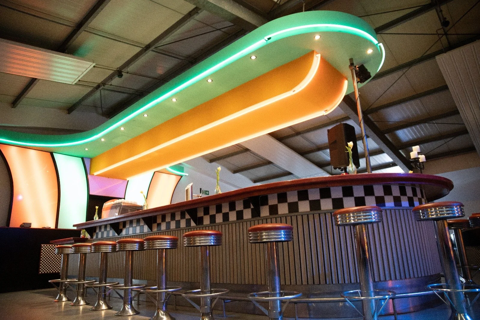 Leeres Bar mit bunten Lichtelementen, Barhockern aus Metall mit rotem Sitzpolster, und einer Theke im Retro-Stil.