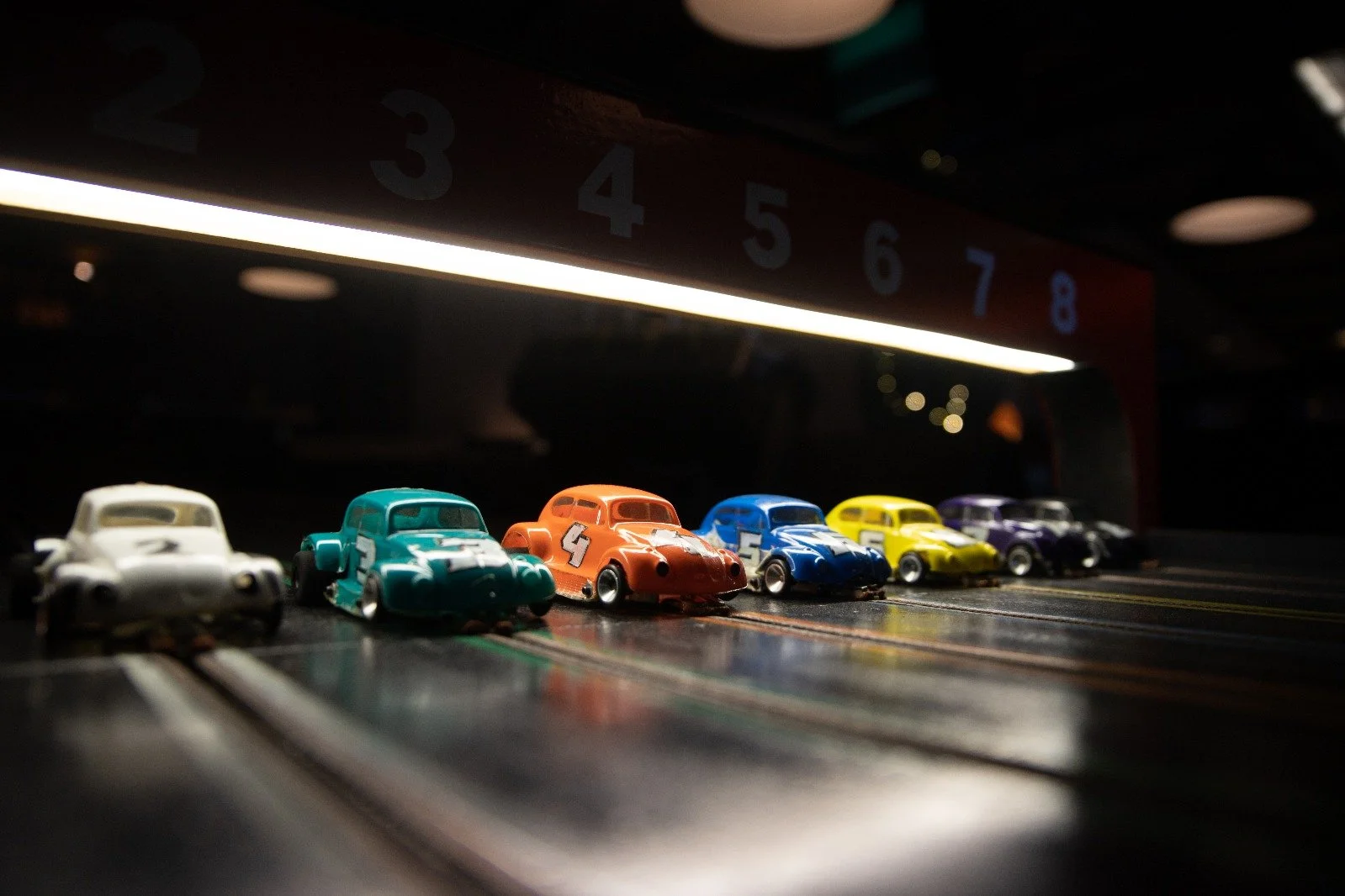 Miniaturmodelle von Rennwagen in verschiedenen Farben auf einer Rennbahn, mit einer Zeitskala im Hintergrund.