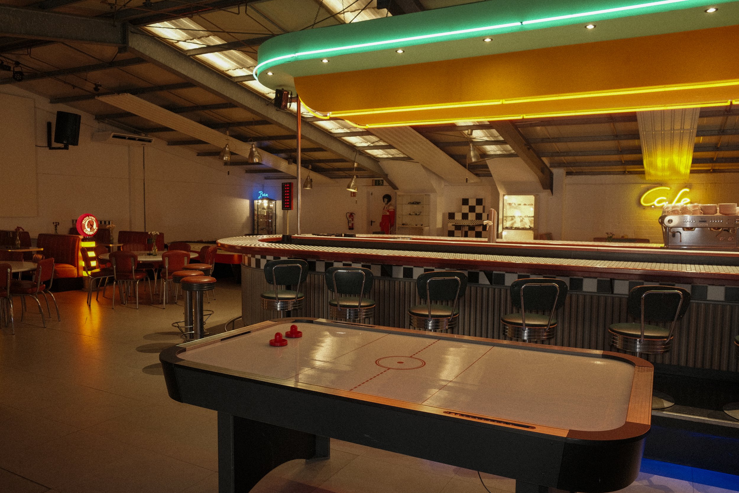 Leeres Sportsbar mit Eishockey-Tisch und Bar im Hintergrund, bunte Neonlichter, gemütliche Sitzgelegenheiten und Dekoration im Retro-Stil.