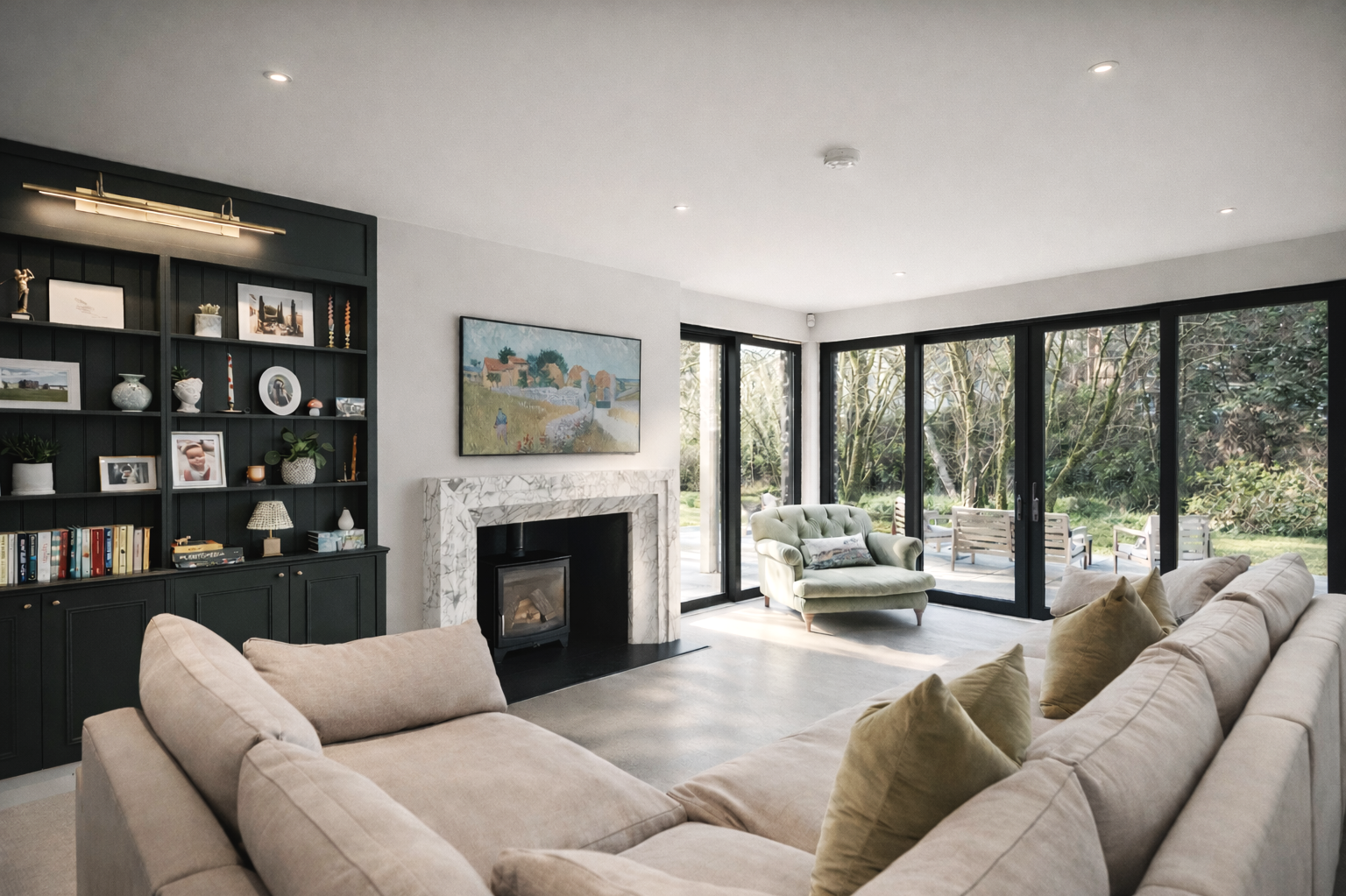 Living room with beige sectional sofa, black built-in bookshelf, marble fireplace, and large glass sliding doors leading to outdoor seating and greenery.