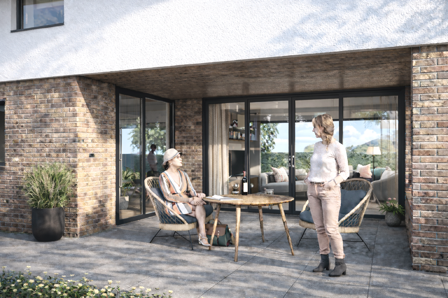 Two women conversing on an outdoor patio in front of a modern brick house with glass sliding doors. One woman is sitting at a wooden table, wearing a striped dress and a sunhat, while the other woman stands nearby in a lace top and pink pants. The patio has potted plants and the interior of the house is visible through the doors.