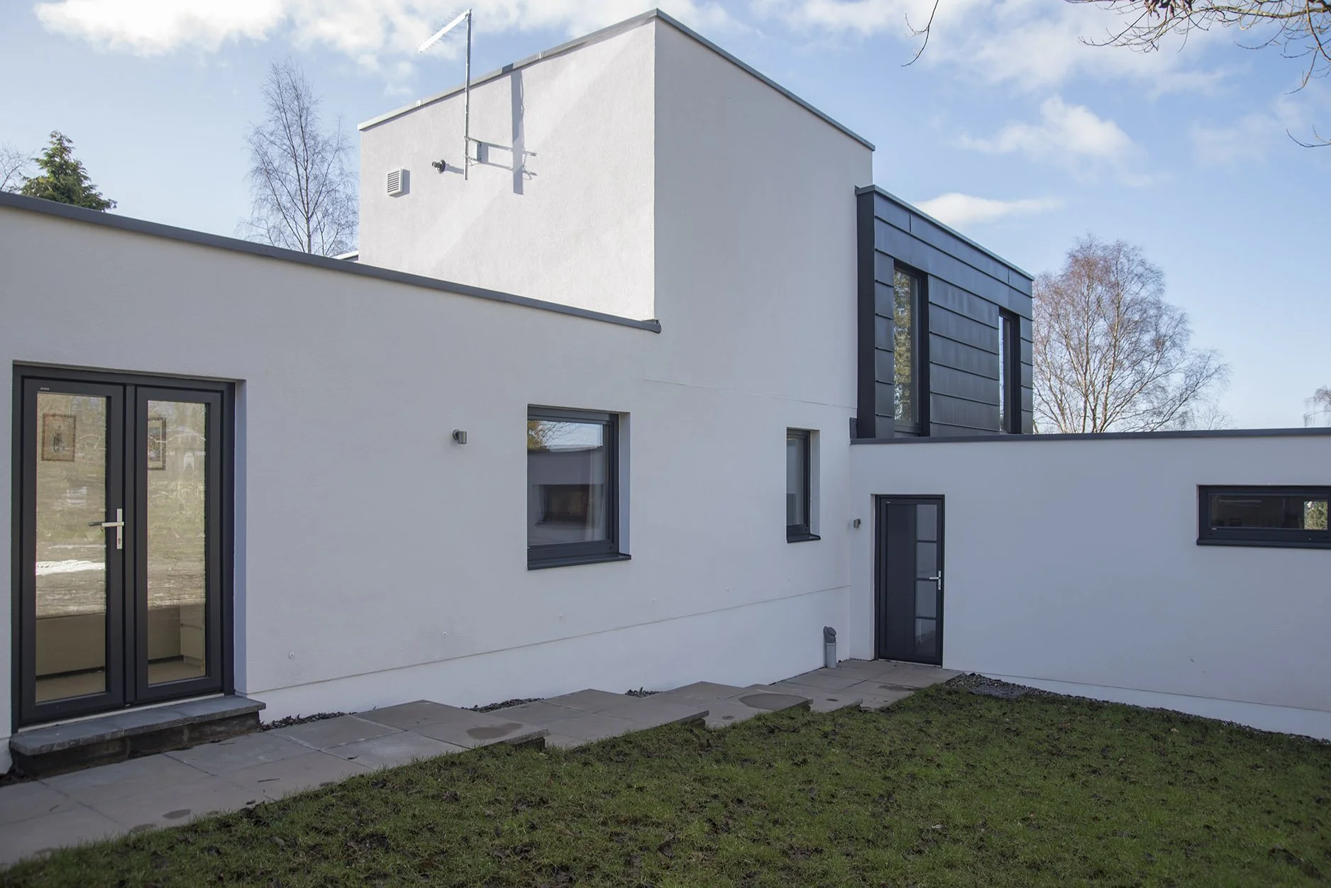 Modern white house with black-framed windows and doors, located on a grassy yard under a blue sky with a few clouds.