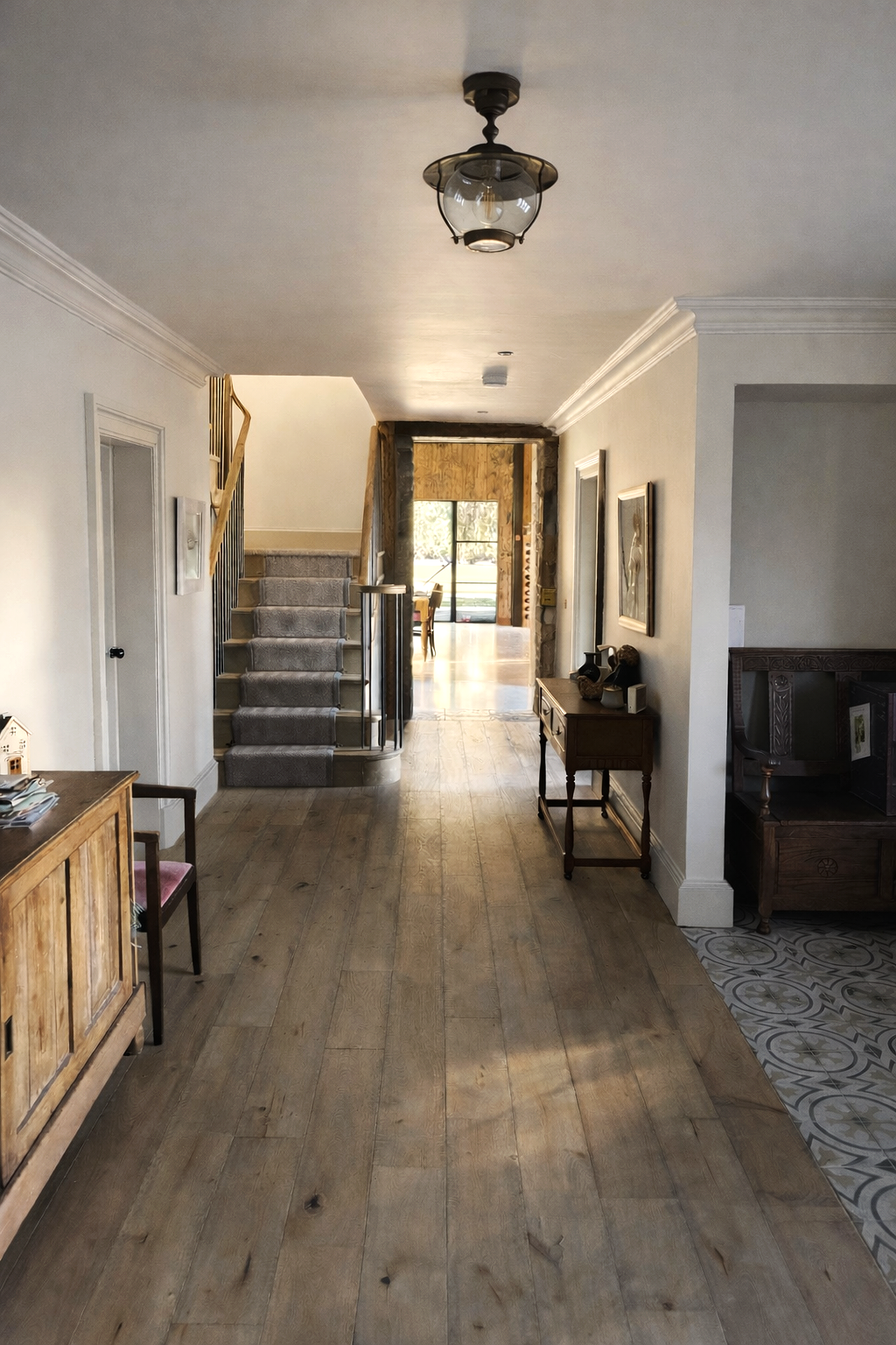 Interior hallway with wooden floor, staircase with gray carpet, and front door leading outside. Walls decorated with artwork and furniture along the sides.