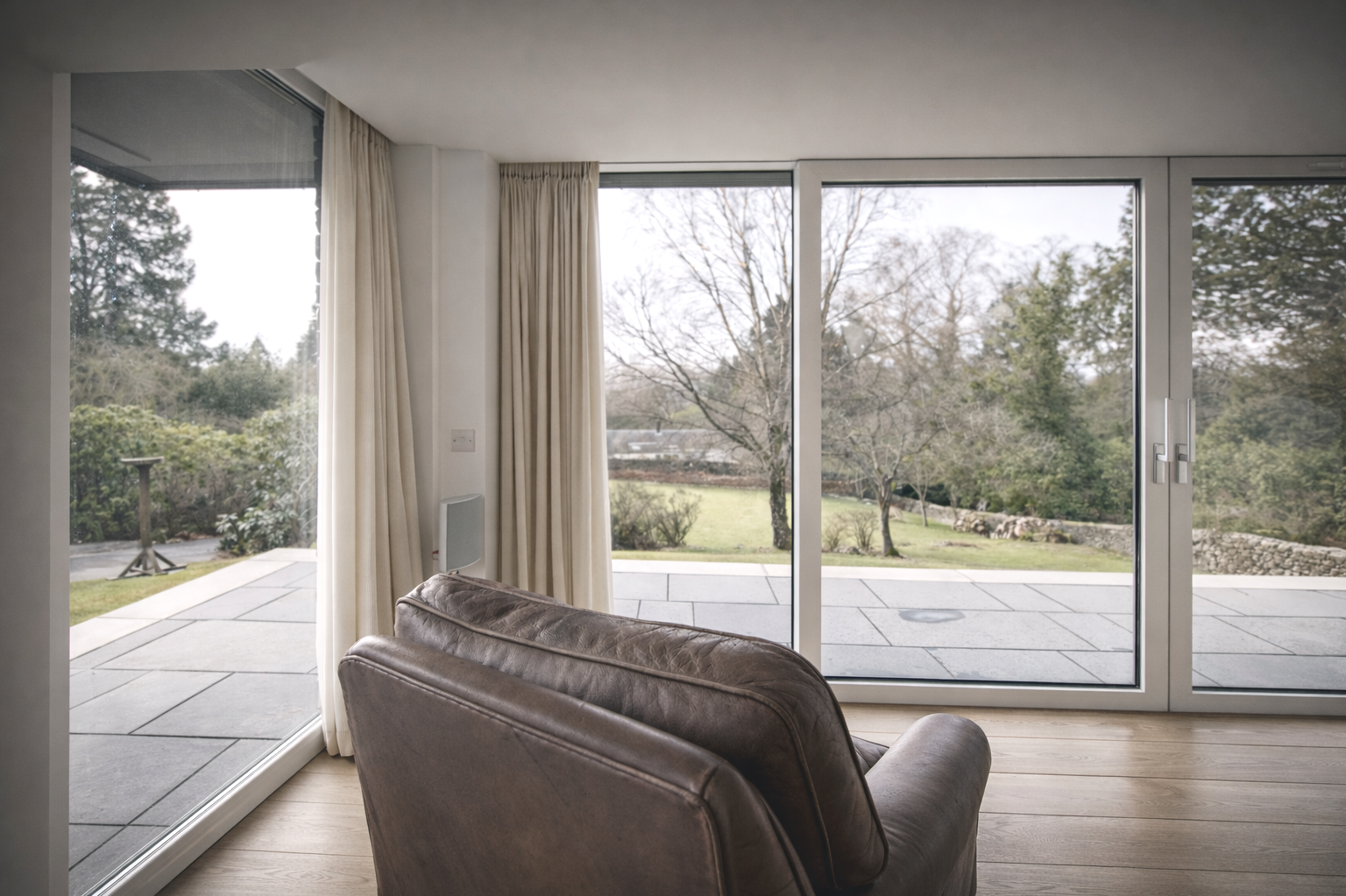 Living room with large glass sliding doors and view of a backyard with trees and a patio.