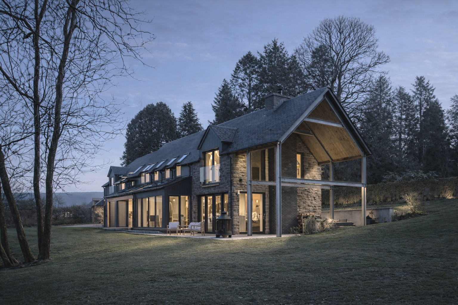 A modern house with large glass windows and a stone facade, situated on a green lawn surrounded by trees during dusk, with interior lights on.