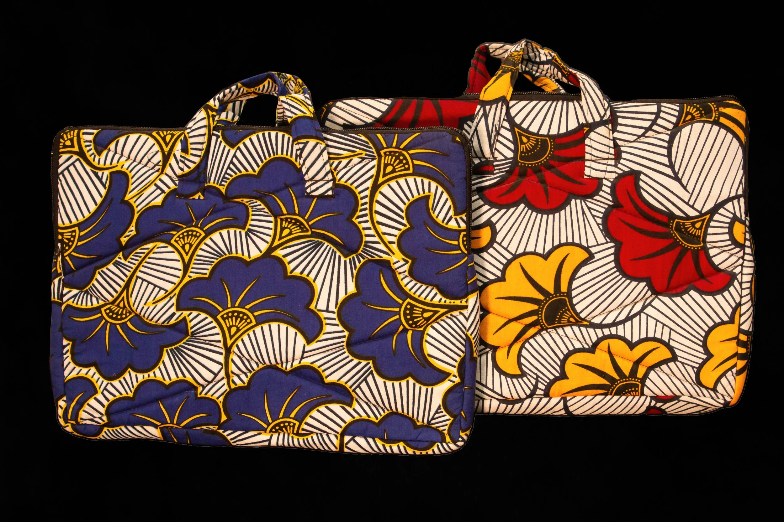 Two large colorful bags with bold floral patterns, one with blue and yellow flowers and the other with red, yellow, and black flowers, against a black background.
