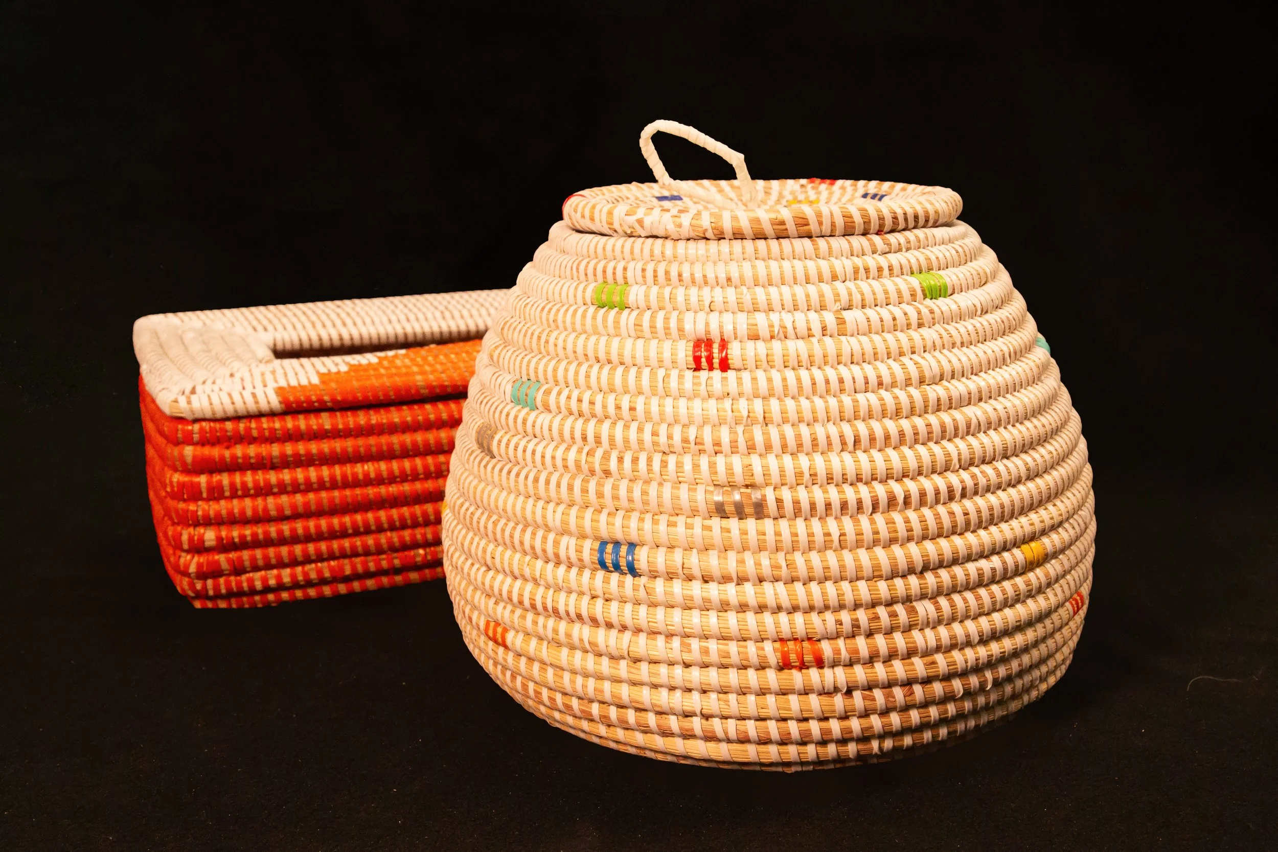 Colorful woven baskets, one round with a handle on top, and one rectangular, placed against a solid black background.