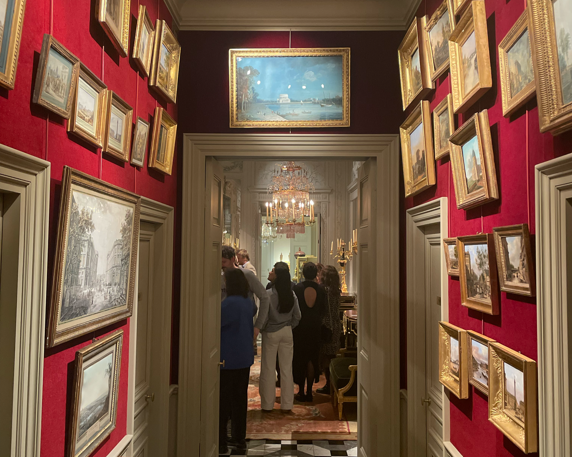 Salle d'exposition avec bustes en marbre, cadres de peintures, cheminée en marbre noir, mur orné de moulures, fenêtres avec rideaux ornés, parquet en bois.
