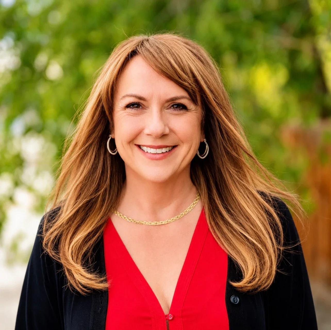 Jean Miller wears a red shirt and black jacket, gold necklace and hoop earrings, and has dark blonde hair