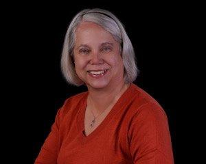 Dorothy Butler is a white woman with short gray hair, a red long sleeve shirt, and is smiling