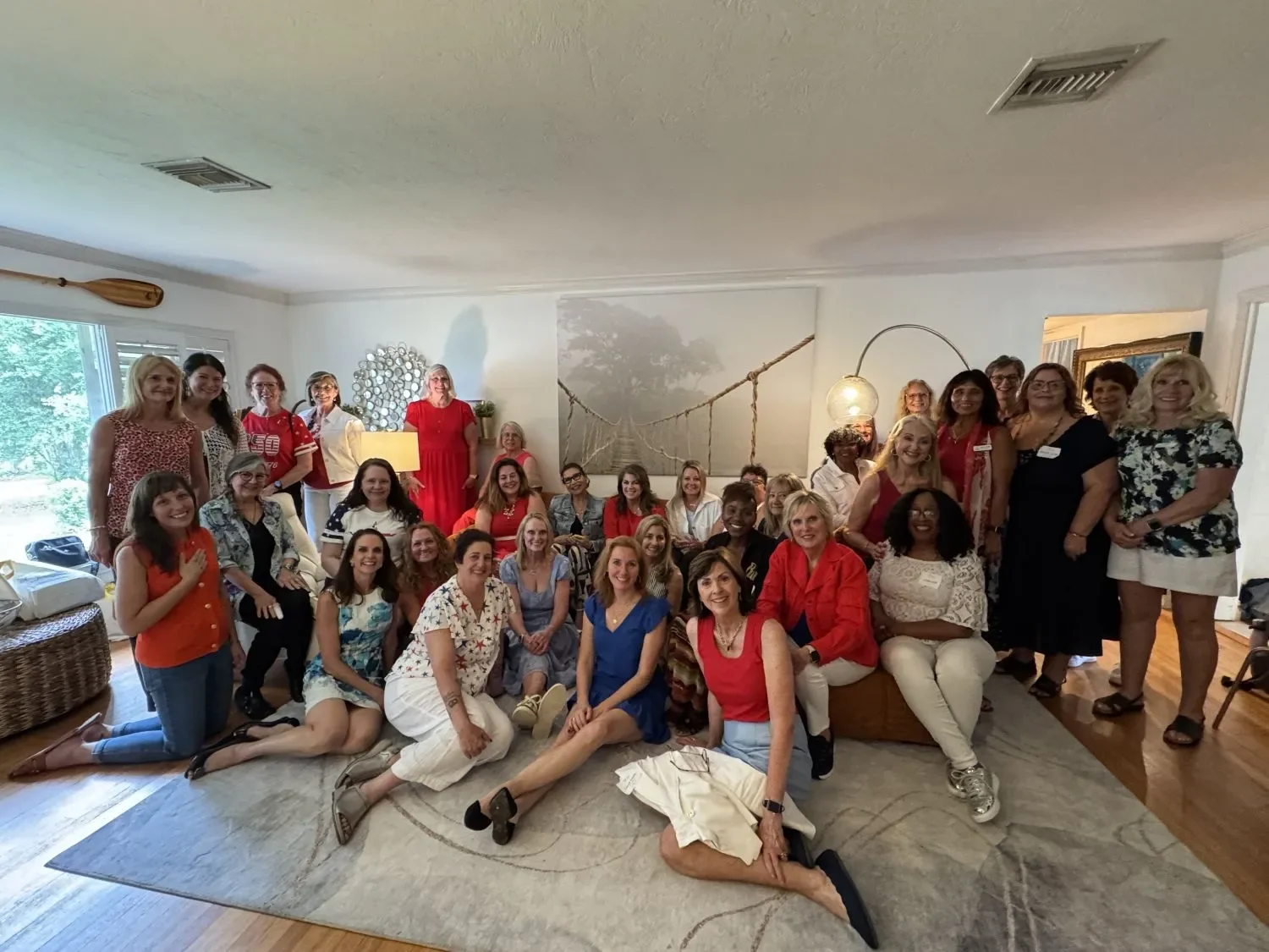 Modern Widows Club group photo at Carolyn's home, with women seated on a couch, some sitting on the floor, and many others standing on either side of them