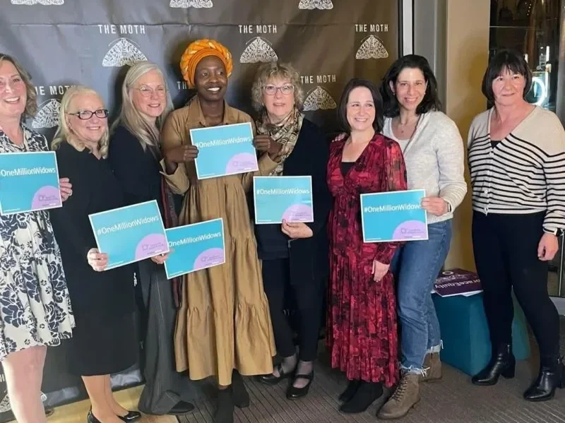 A group of women stand together all holding signs that read #OneMillionWidows