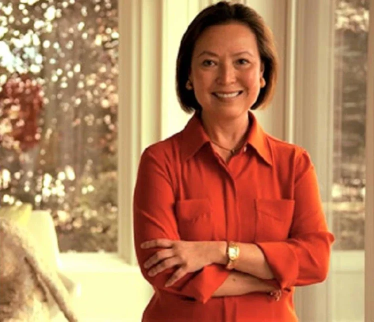 Angelica wears a bright red button down shirt and stands with her arms crossed in front of her, smling at the camera.