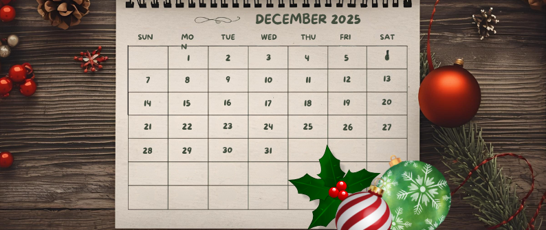 December 2025 calendar on a wooden table surrounded by Christmas decorations including ornaments, holly, pine branches, and berries.