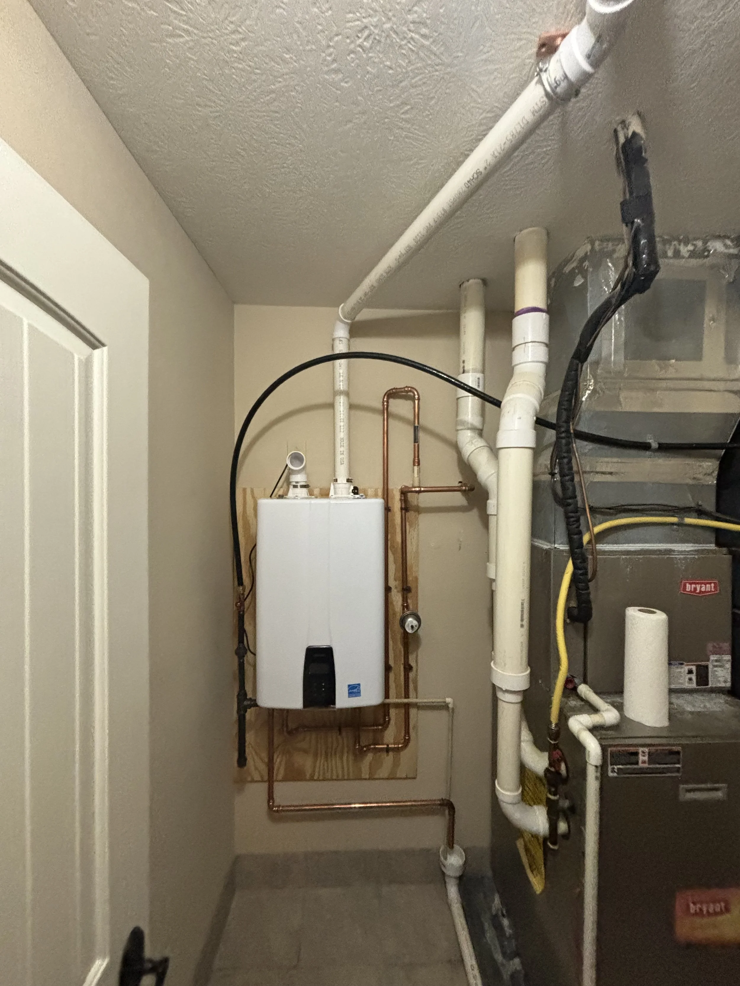 Navien tankless water heater installation by RonJon Plumbing in Delaware, Ohio, showing copper water lines, expansion tank, secured gas line, and venting through attic to roof.