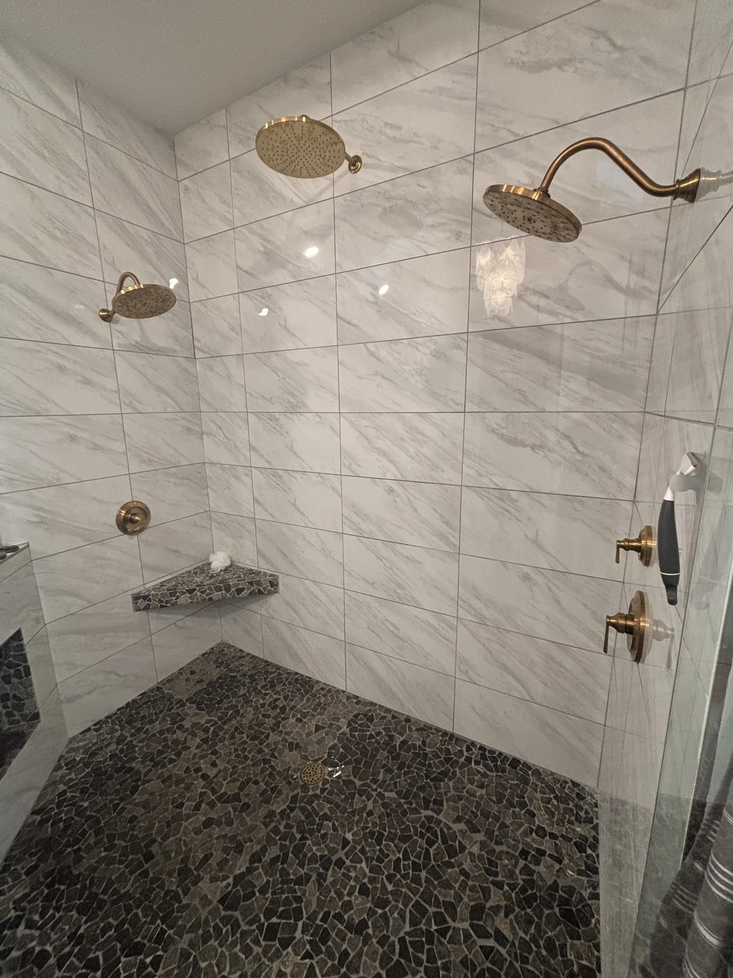 Luxury bathroom remodel in Delaware, Ohio, featuring dual shower valves, diverter, gold finish trim, rain head, and wall-mounted shower head installed by RonJon Plumbing.