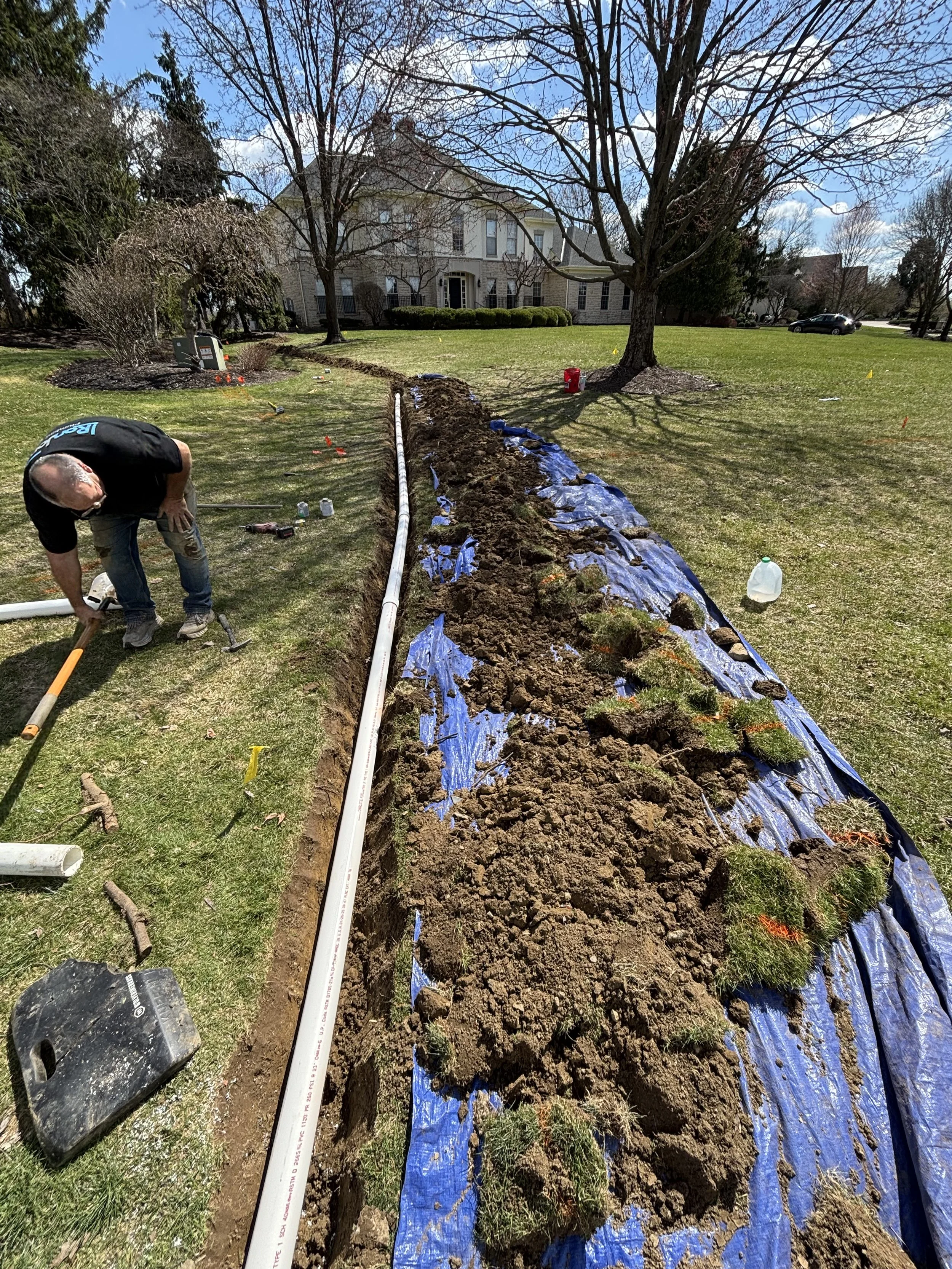 Yard drain replacement by RonJon Plumbing in New Albany, Ohio, showing new PVC drain line and tarps protecting soil and grass during excavation.