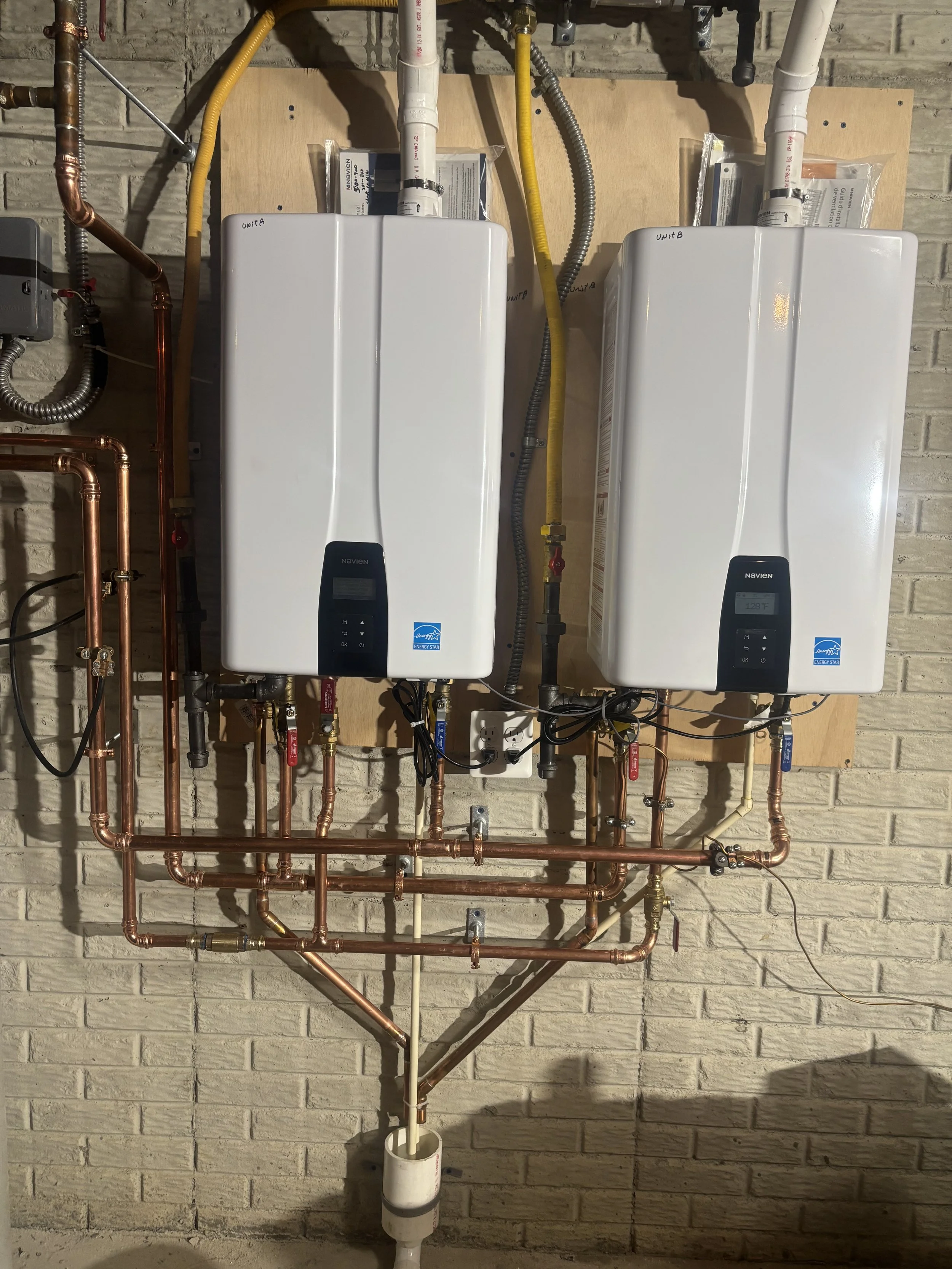 Dual Navien tankless water heater installation by RonJon Plumbing in Westerville, Ohio, featuring copper water lines, gas lines, venting, and a new condensate drain — neatly mounted and secured to the wall.