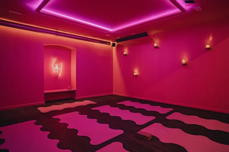Salle de yoga ou méditation avec éclairage rose vif, tapis de yoga au sol, bougies allumées sur les murs, ambiance relaxante et moderne.