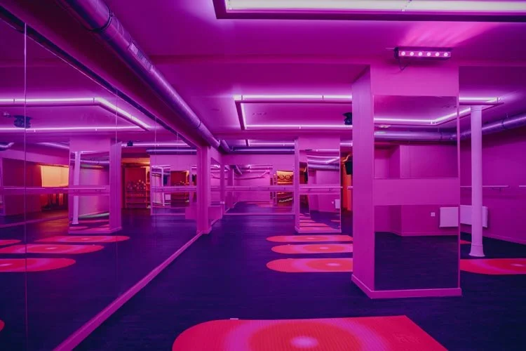 Salle de sport ou studio de fitness avec éclairage violet et planches de yoga éclairées en rouge.