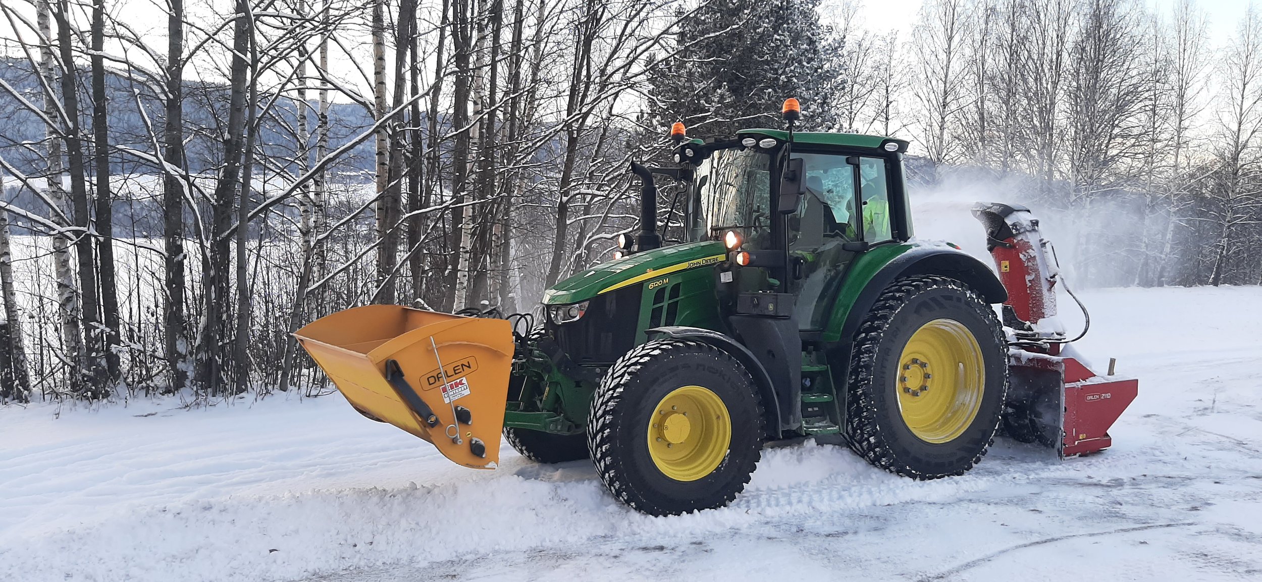 Traktor med snøplog og snøfreser som rydder snø på en vinterdag, omgitt av snødekte trær.