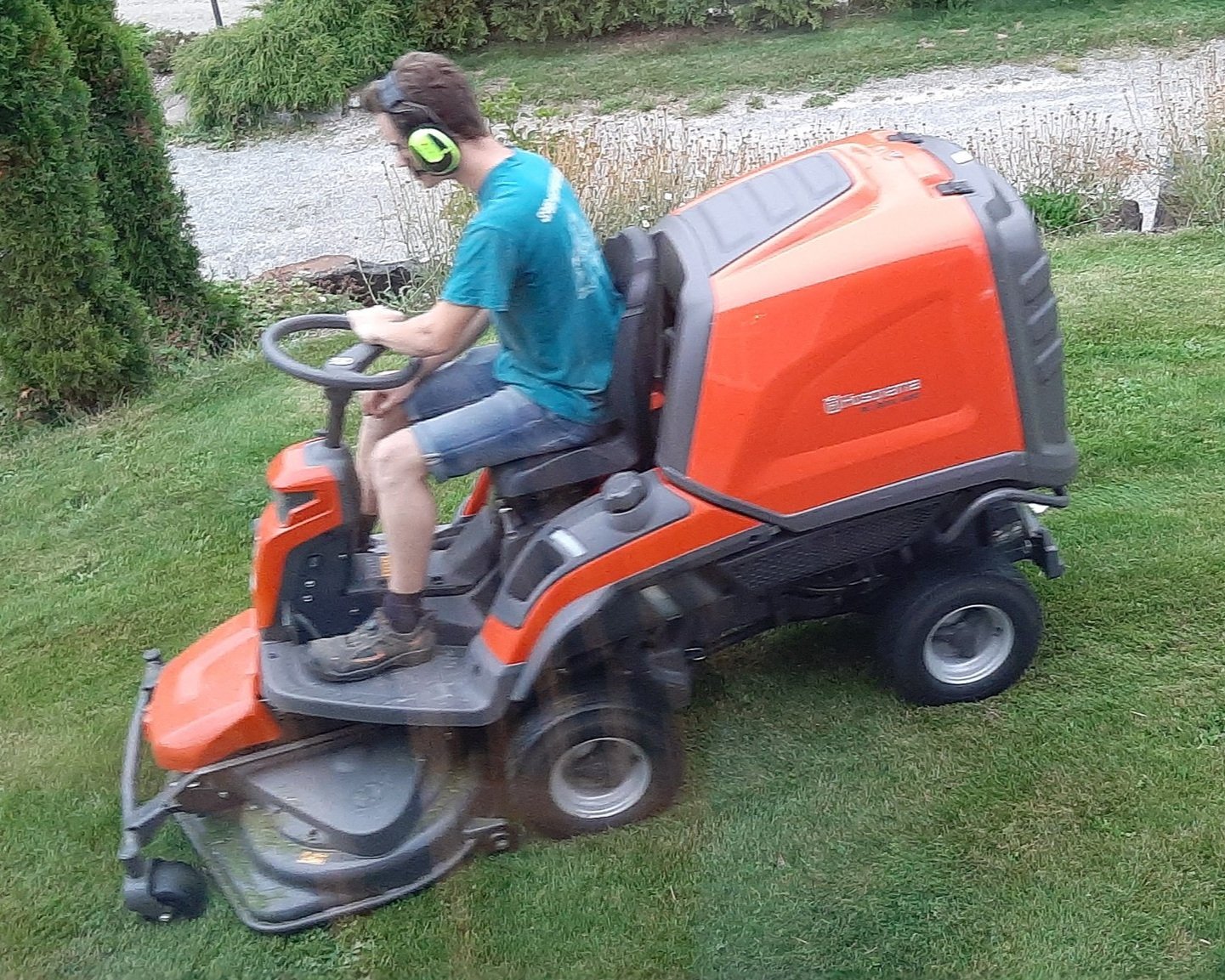 Person som kjører en orange gressklipper på en grønn plen i en hage