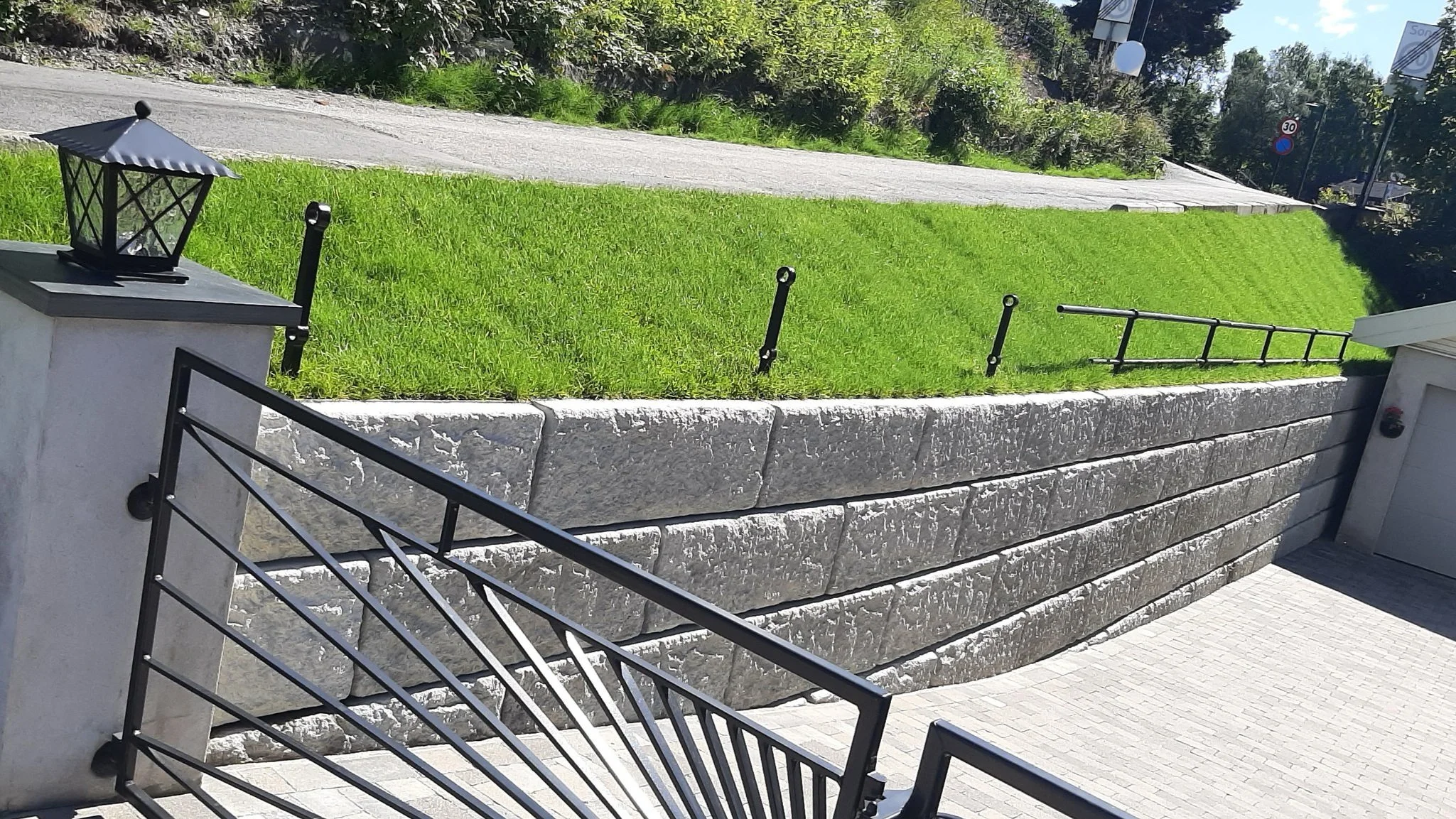 Trapp og mur som omkranser en hage med grønt gress og en vei i bakgrunnen.