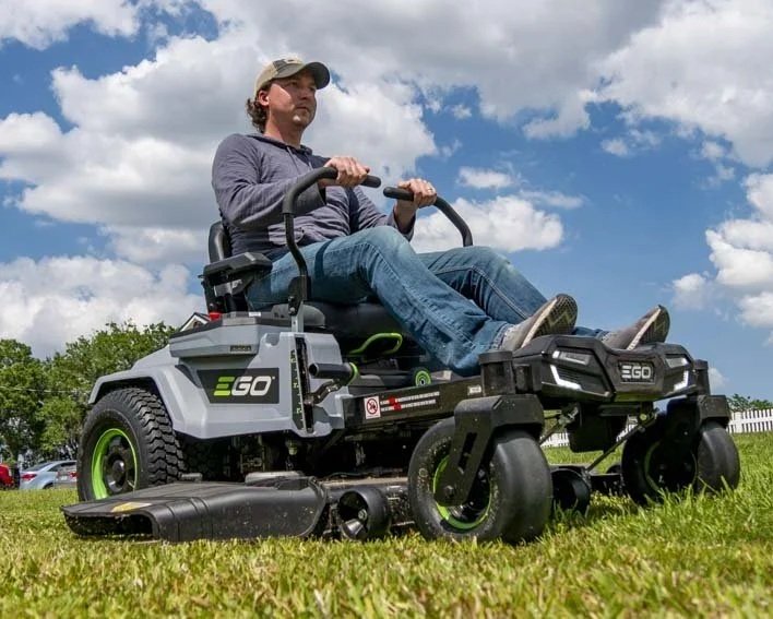A man sitting on a riding lawn mower in a grassy yard on a partly cloudy day.