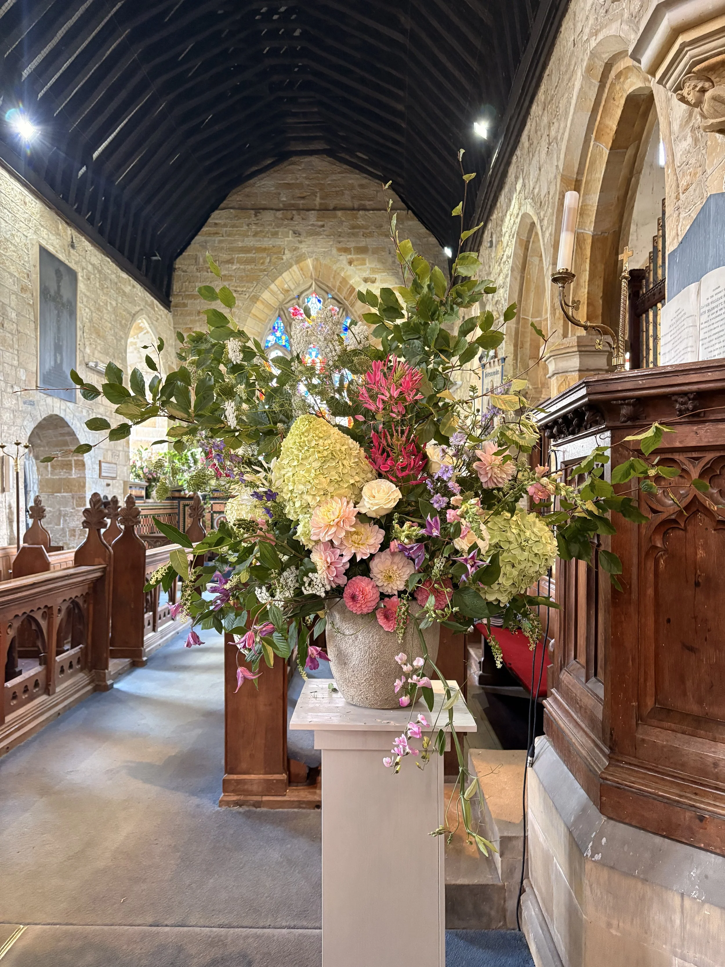 Colorful flower arrangement in a church interior with stained glass windows and wooden pews.