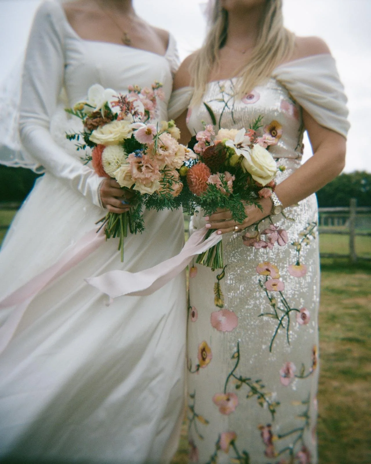 Two women in wedding dresses holding bouquets of flowers, standing outdoors.