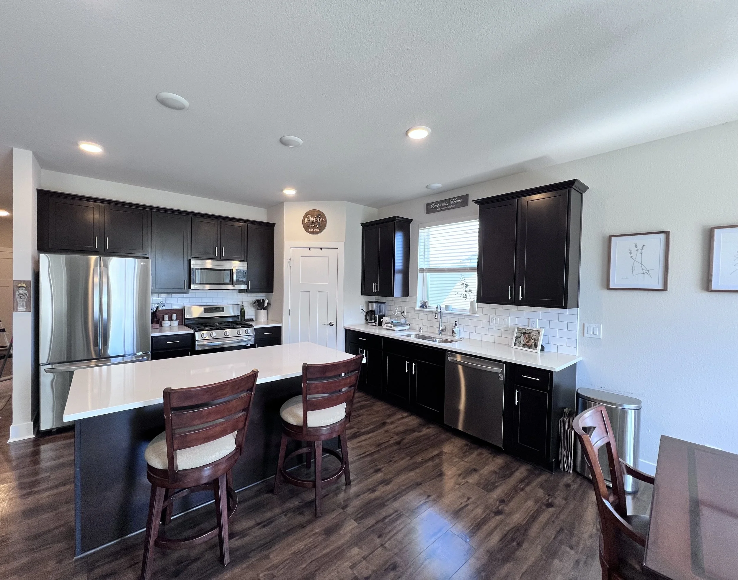 Modern kitchen with dark cabinets, stainless steel appliances, white countertop island, and wooden flooring.