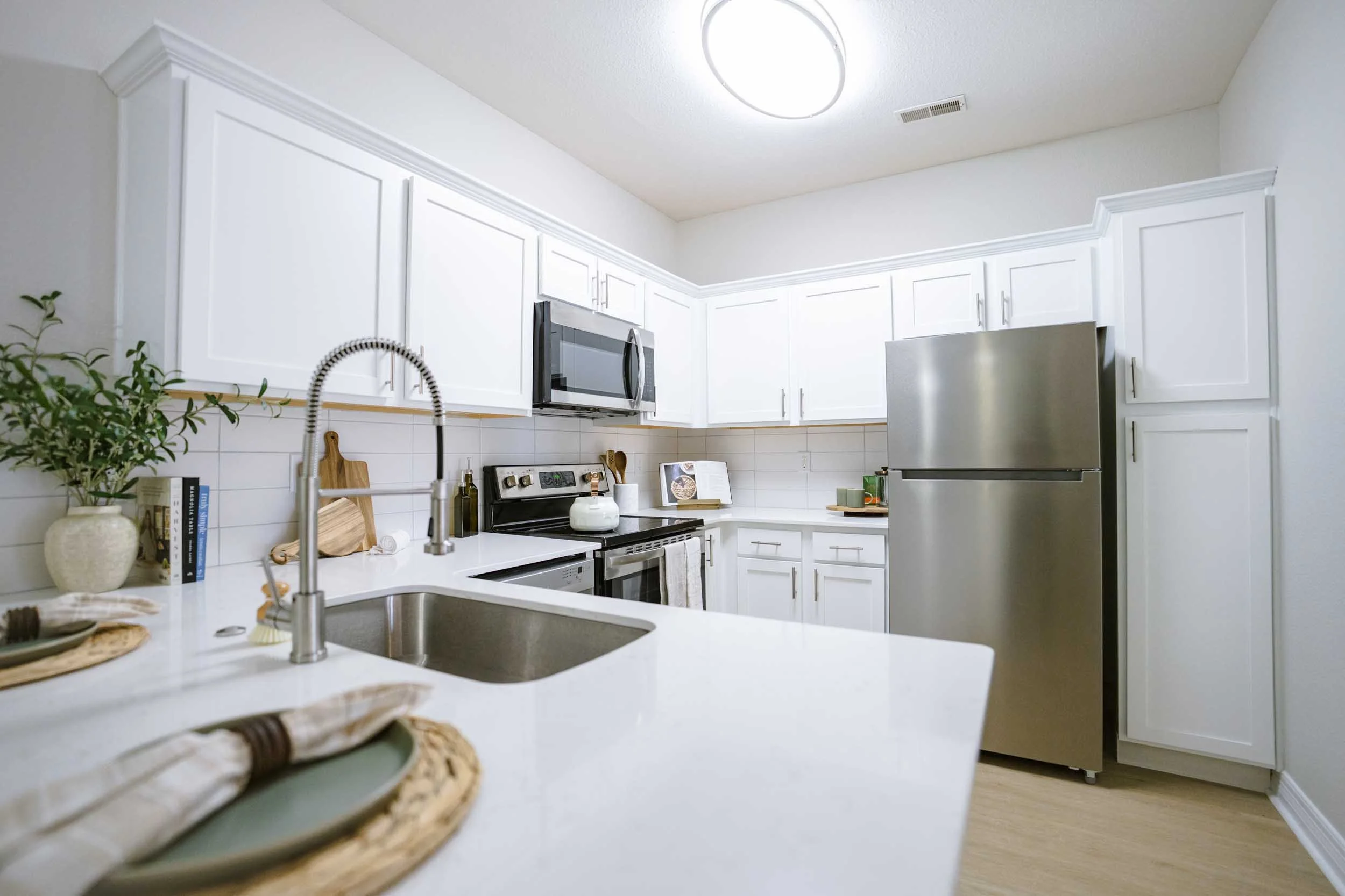 Kitchen with white cabinets, stainless steel appliances, a black stove, and a white countertop with decorative items, a potted plant, and a woven tray.