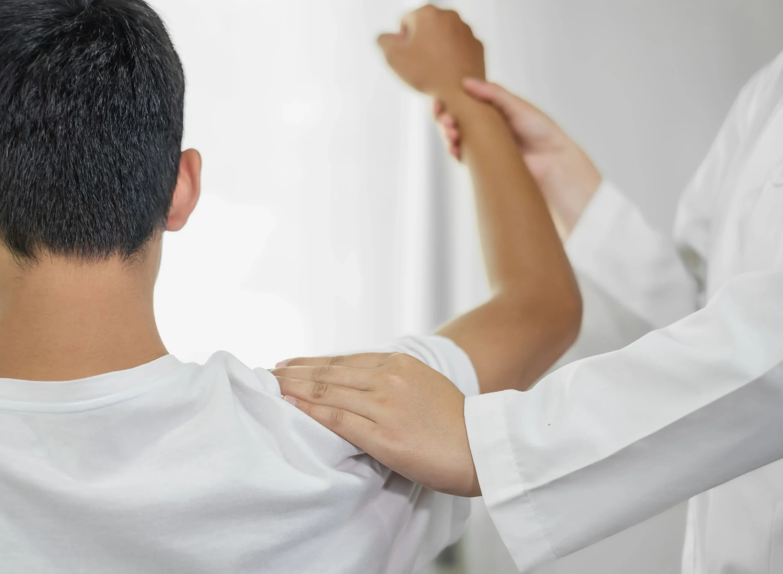 A healthcare professional with white coat examining a patient's shoulder.