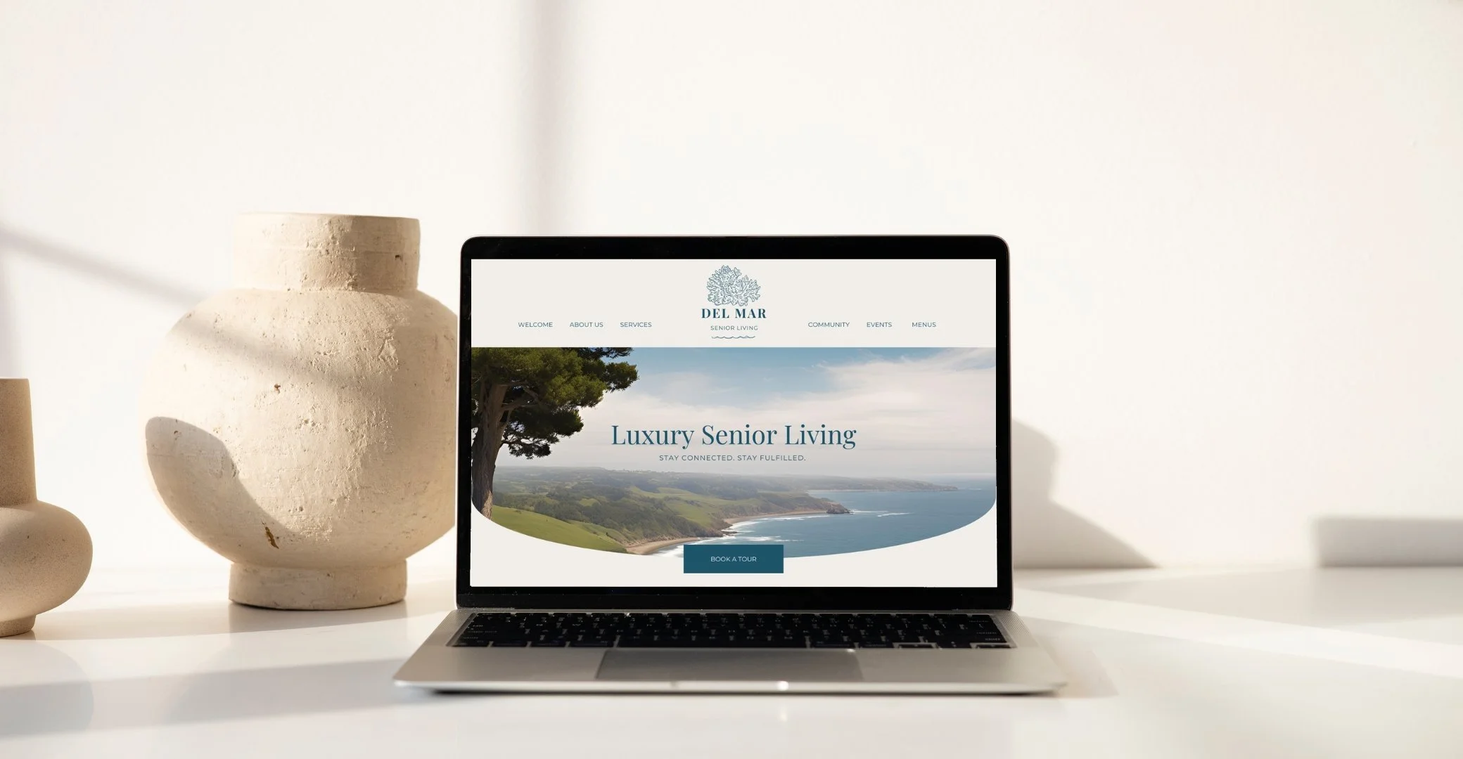 Laptop displaying "Luxury Senior Living" webpage on a white desk with pottery decor.