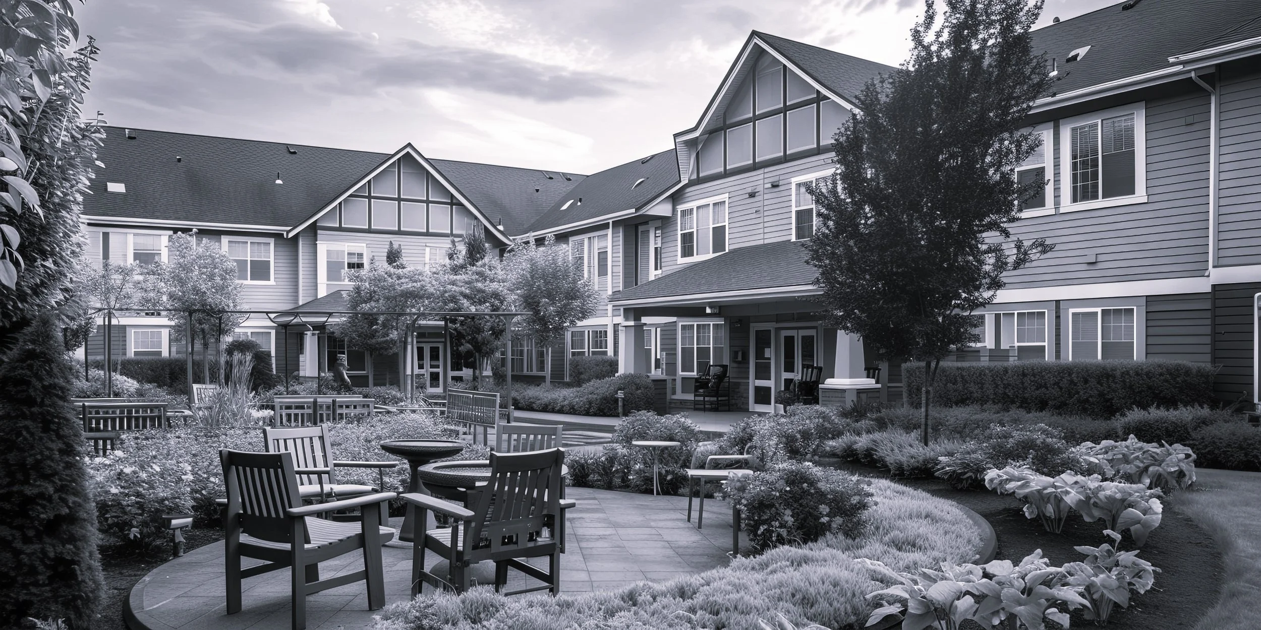 Outdoor courtyard with chairs and tables surrounded by greenery in front of a large residential building.