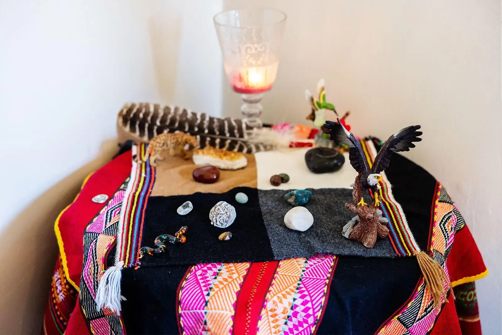 A small altar with colorful woven cloth, decorated with jewelry, stones, figurines, and a lit candle.